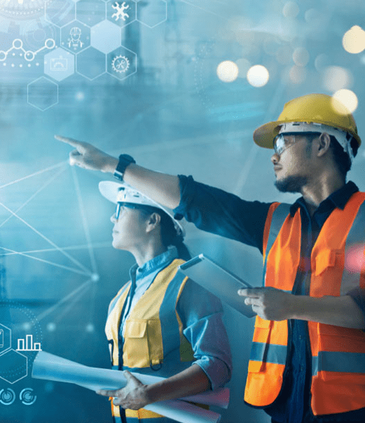 Two construction workers in safety vests and hard hats, one holding blueprints and the other pointing upwards, standing in front of a holographic display of various abstract digital icons and graphs representing data and connectivity.